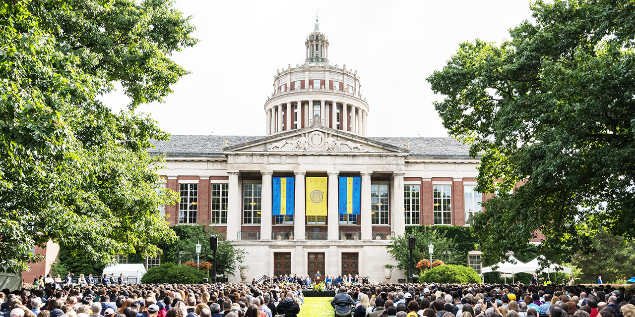 An audience of people seated in front of the Rush Rhees Library