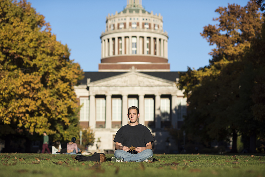 A student sitting crosslegged on the quad with their eyes closed.