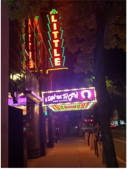 An exterior view of the Little Theater sign lit up at night.