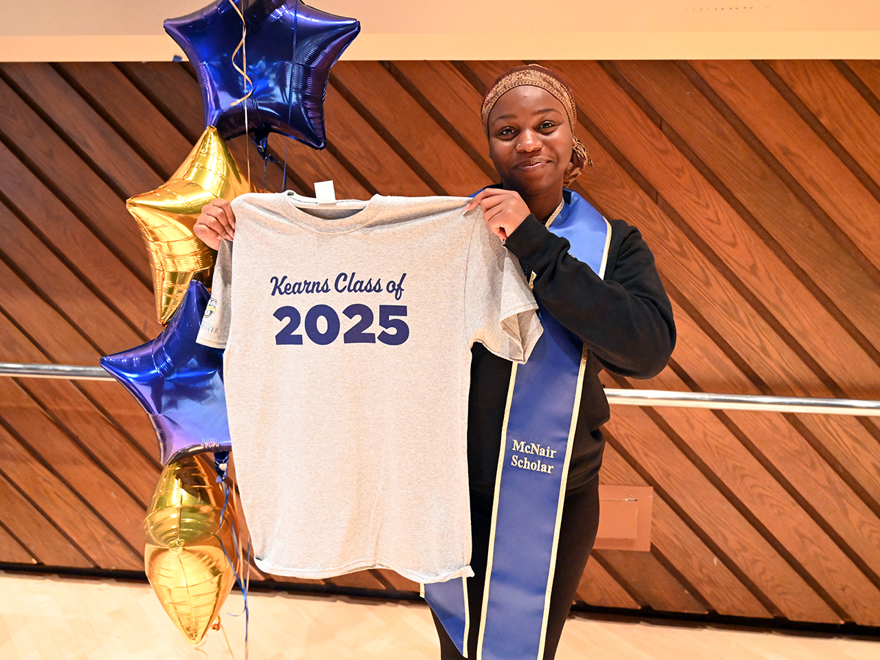 Rosebell Onuma holds up a t-shirt that says Kearns Class of 2025.