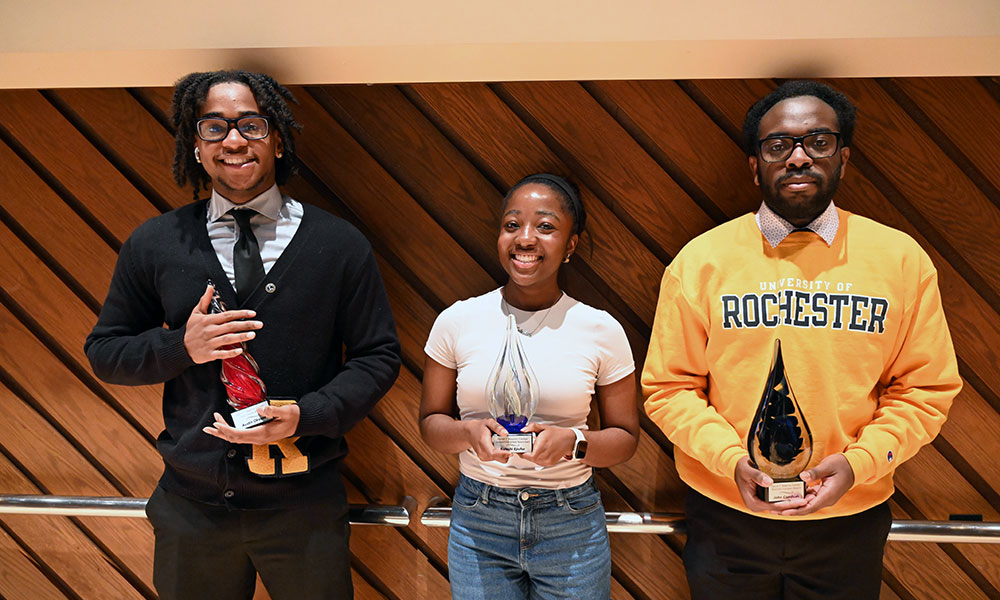 Three students holding their awards and smiling at the camera.