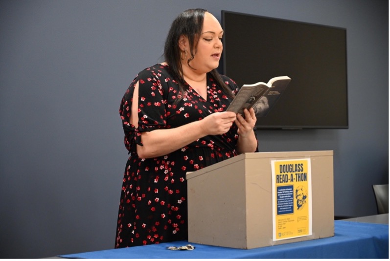 A person reading aloud from a book behind a podium.