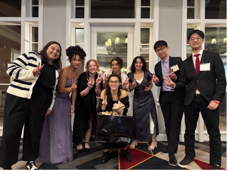 A group of students in dress clothes smiling at the camera and making peace signs with their hands.