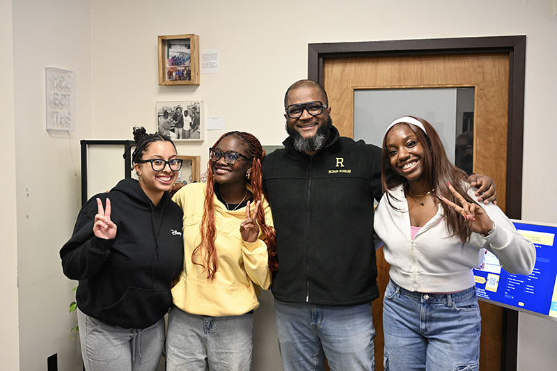 Four people smiling at the camera holding up their fingers in peace sign.