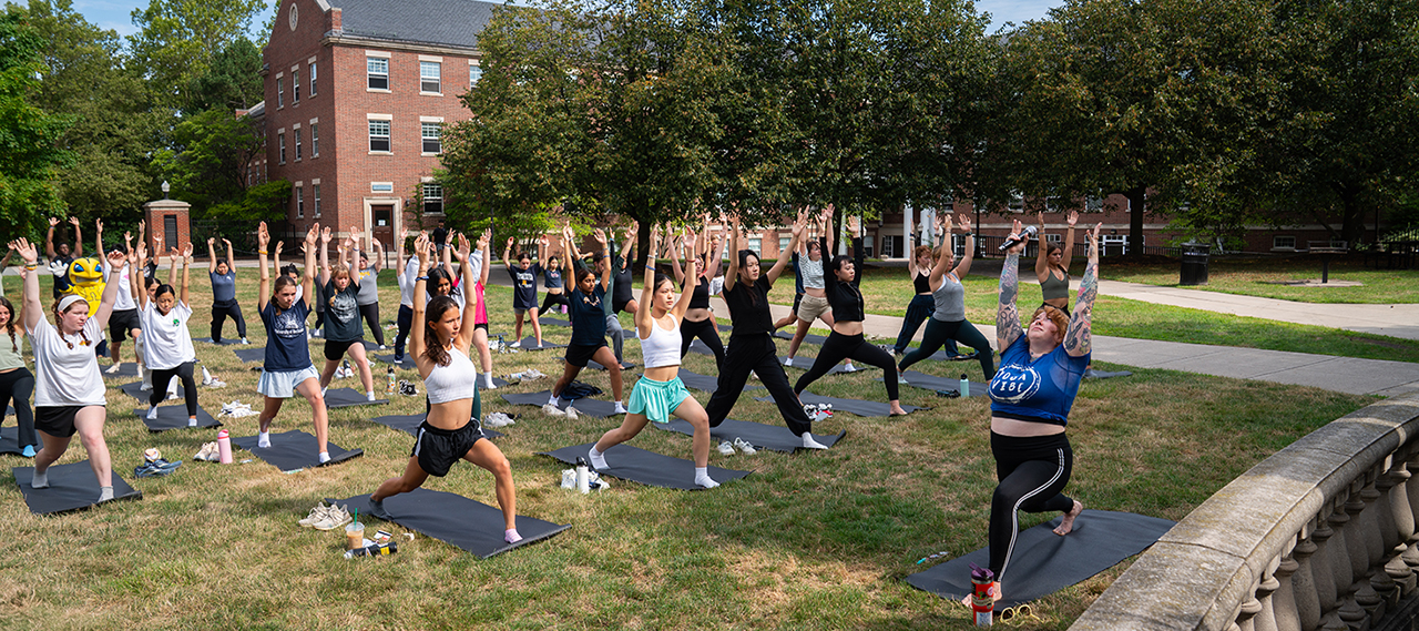 A large group of students practicing yoga outside on Wilson Quad with our mascot, Rocky.