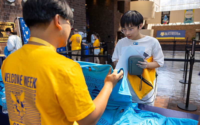 Photo of a student staff member helping a new student select a t-shirt at Welcome Week Check-In