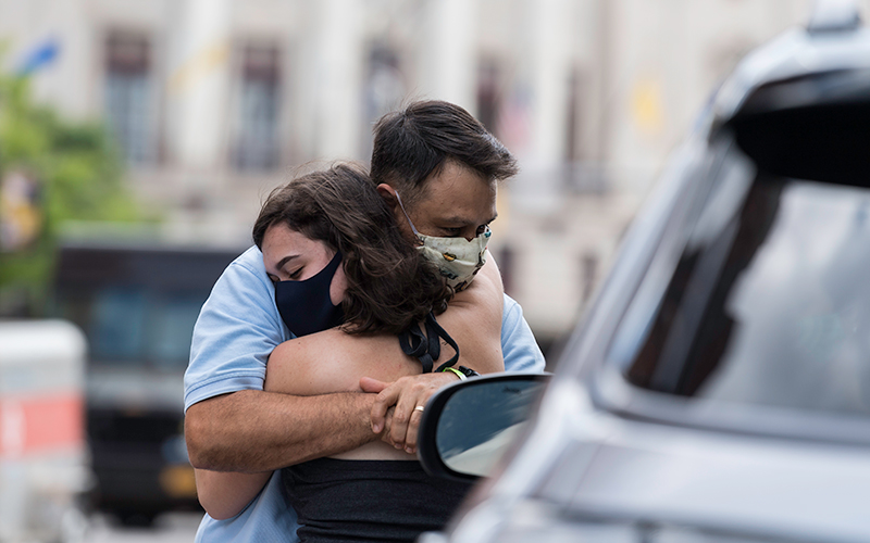 Photo of a student and their parent hugging with a vehicle in the foreground