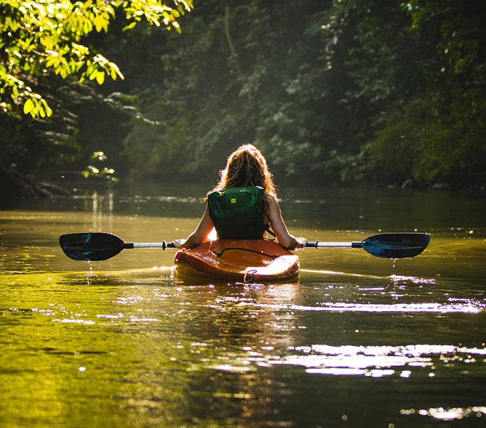 Photo of a women floating in a kayak along a river surrounded by trees