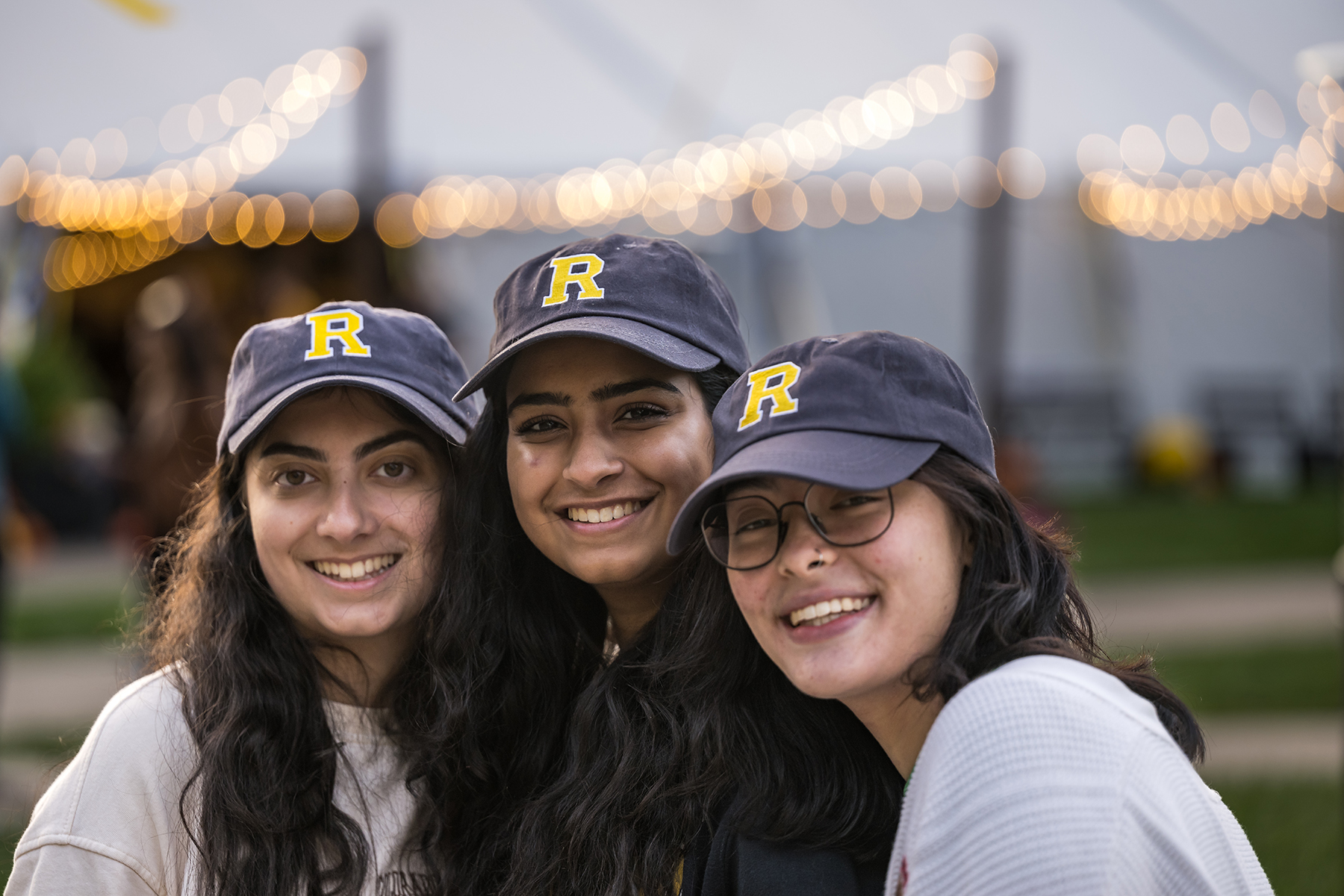 Students in Rochester baseball hats smile and pose with sparkling lights behind them