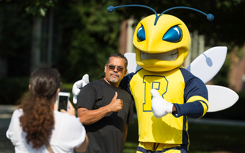 A parent poses with a thumbs up standing next to Rocky, while another parent takes a photo on their phone
