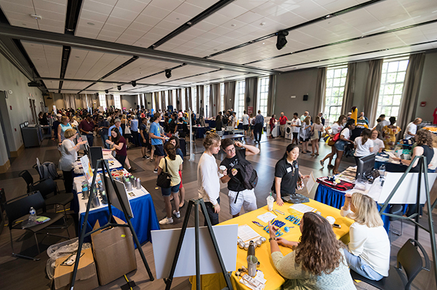 Photo of students and staff interacting at tables set up in Feldman Ballroom