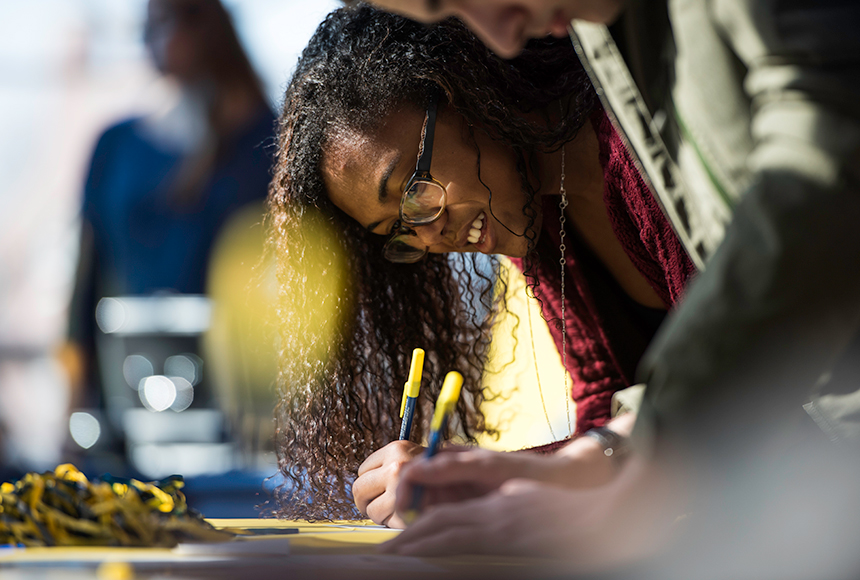 Photo of students leaning over a table and writing