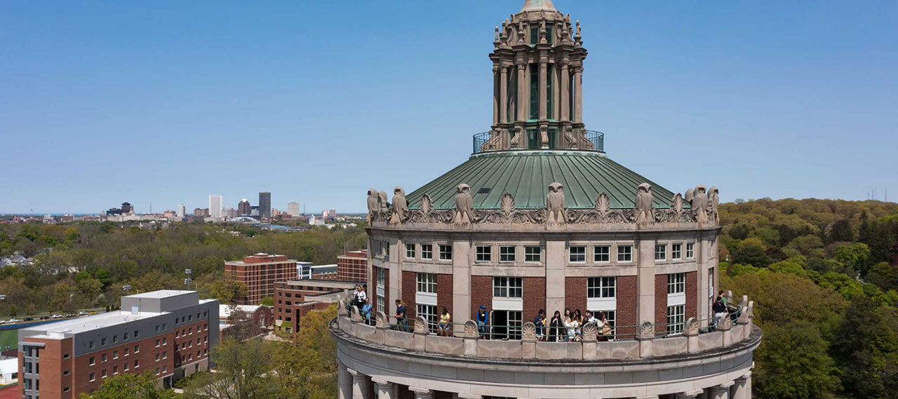 Drone photo of the Rush Rhees Library tower with the City of Rochester skyline in the background.