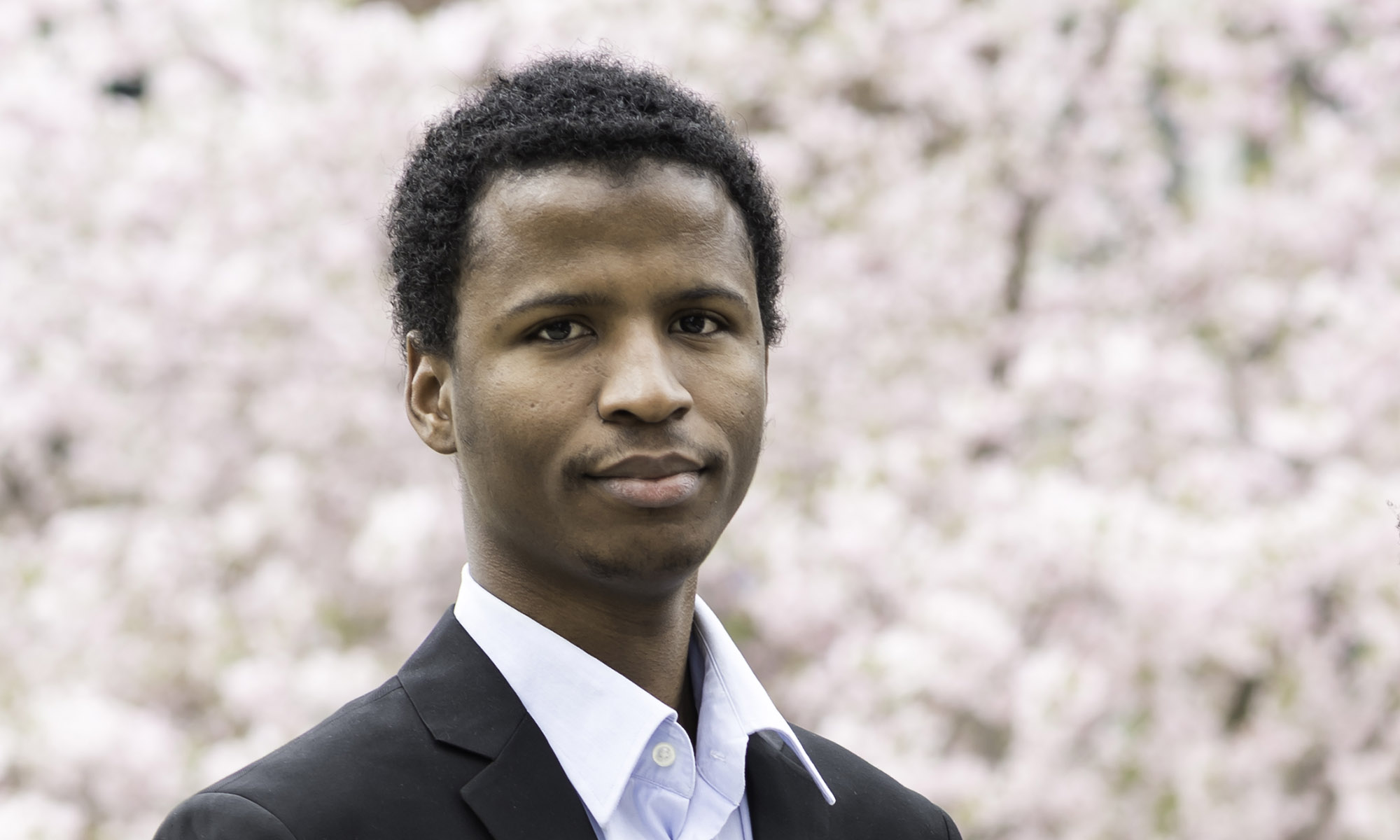 Souleymane Diallo poses in front of backdrop of cherry tree blossoms.