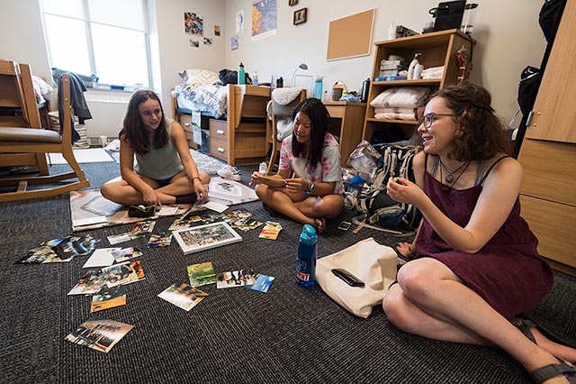 Three students sitting on the floor in a dorm room.