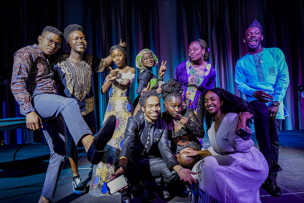 A group of students in traditional garb smiling in colorfully lit room