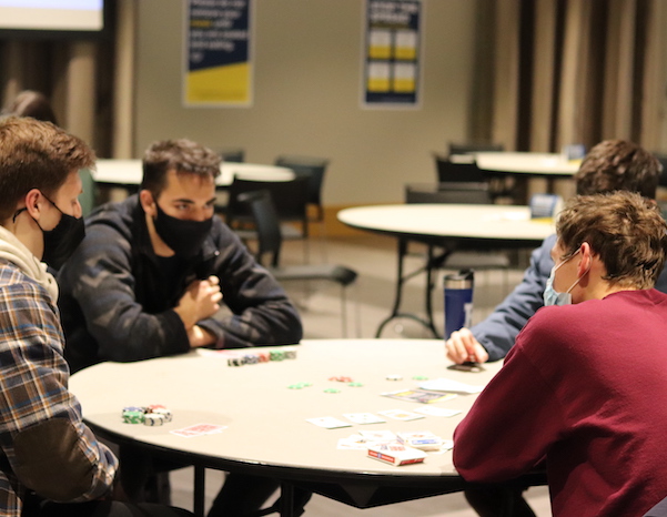 Four masked students at a card table playing a card game with chips