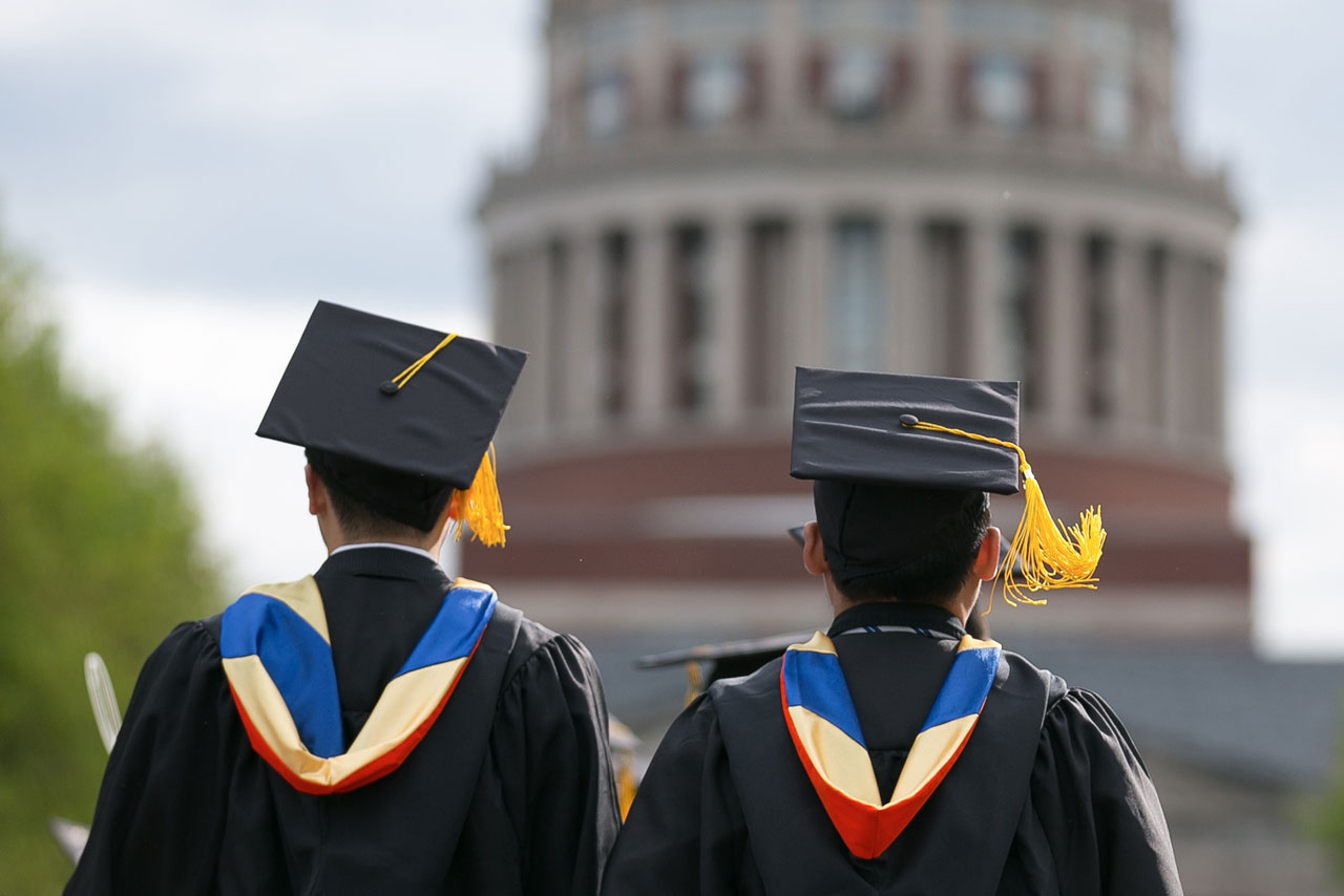 Two University of Rochester graduates walk down the main isle towards the library for their Commencement ceremony