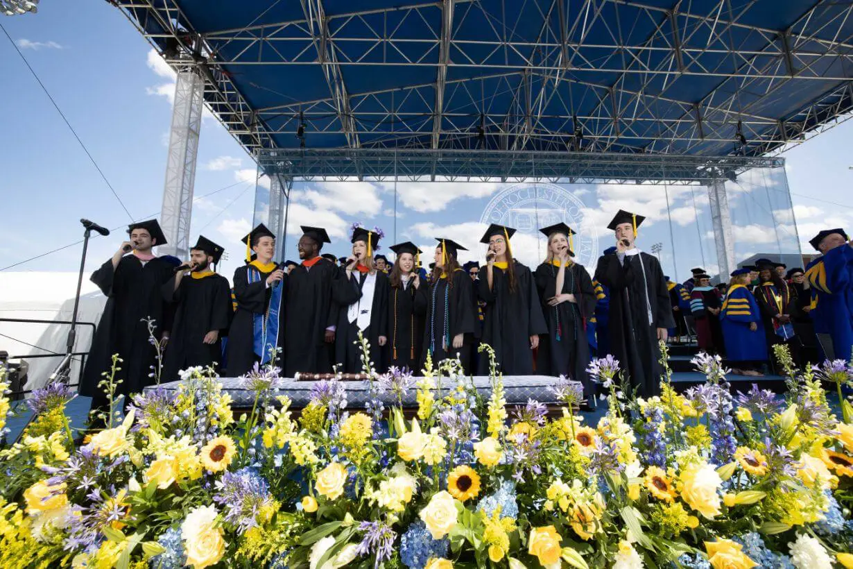 A group of graduates stands before a flower-decorated stage at the University of Rochester Commencement Weekend.