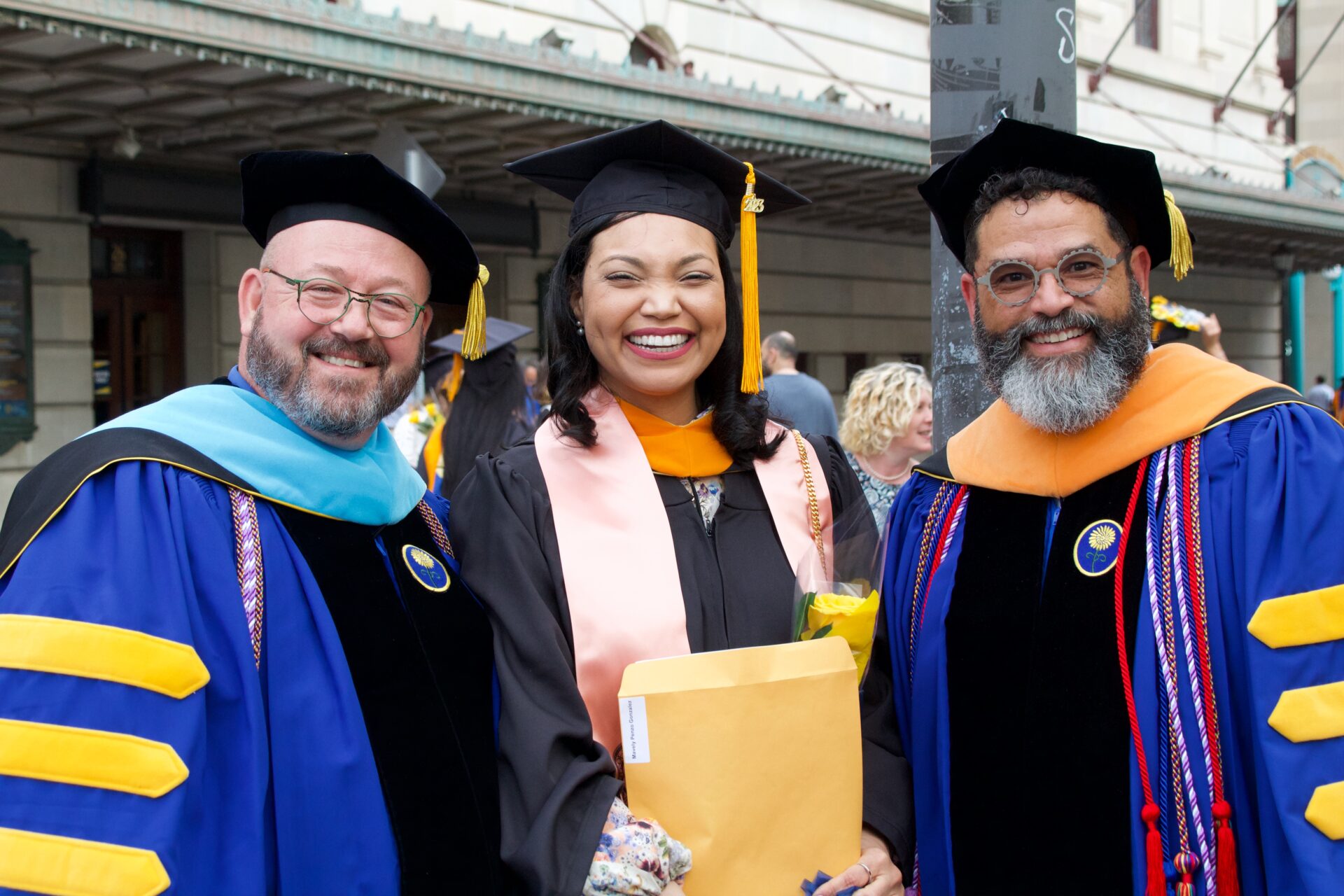 Students and professors celebrate outside the Eastman School of Music in graduation regalia.