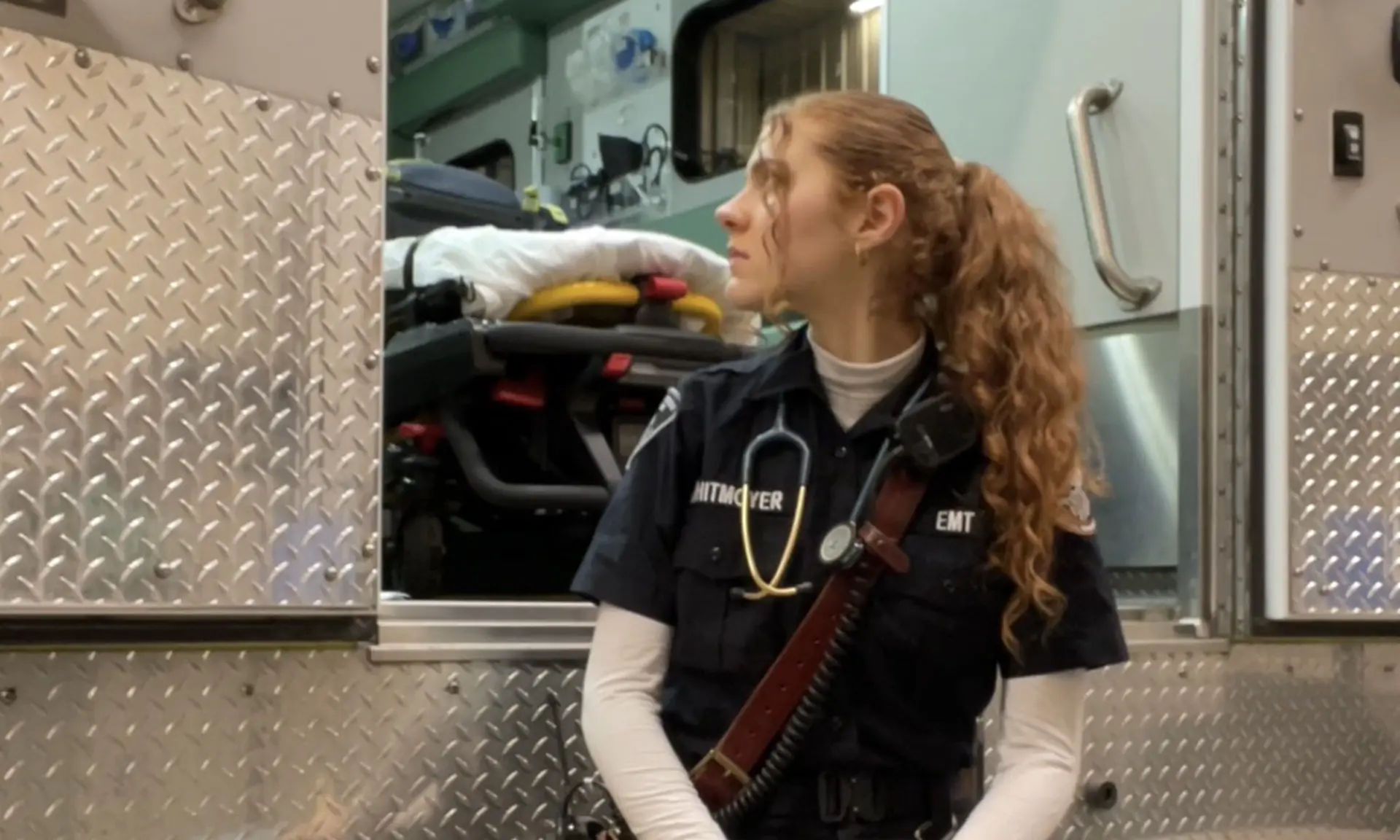 Close-up horizontal of Rachel Whitmoeyer against a black background in an EMT uniform staring at the camera.