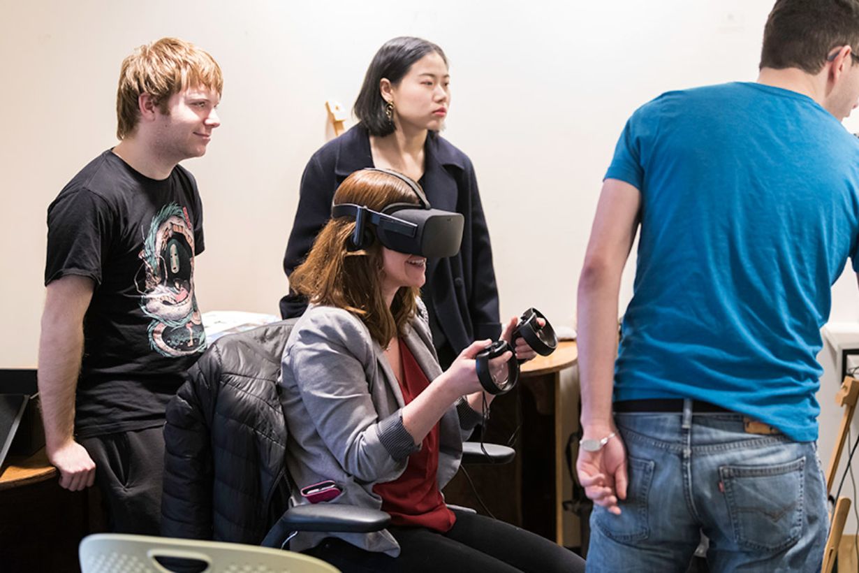 Four students, one in a virtual reality headset, sitting around a computer screen.