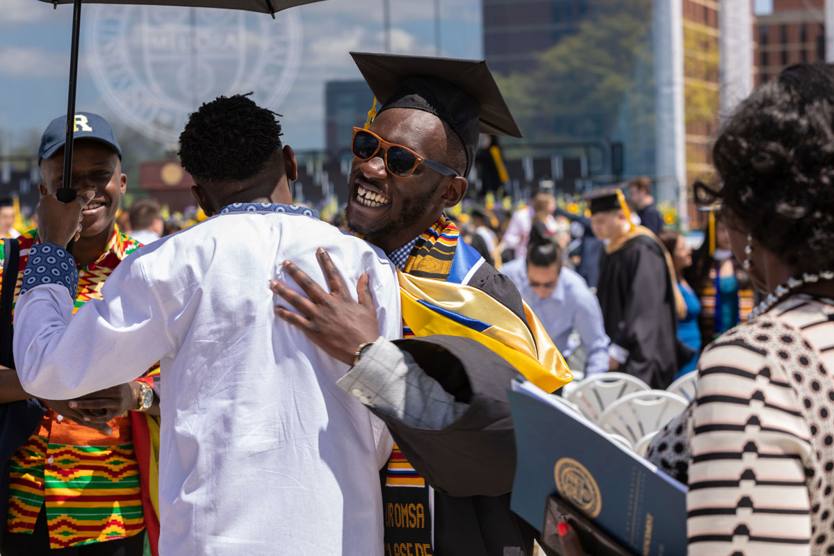 A man in a graduation cap and gown embraces another man during the University of Rochester Commencement Weekend celebration.