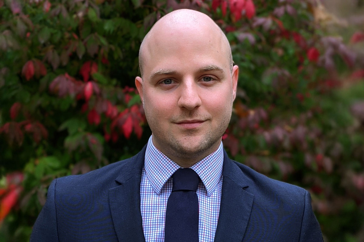 Bald man in a suit and tie stands by a tree, representing University of Rochester Class of 2025 student Michael McCarthy.