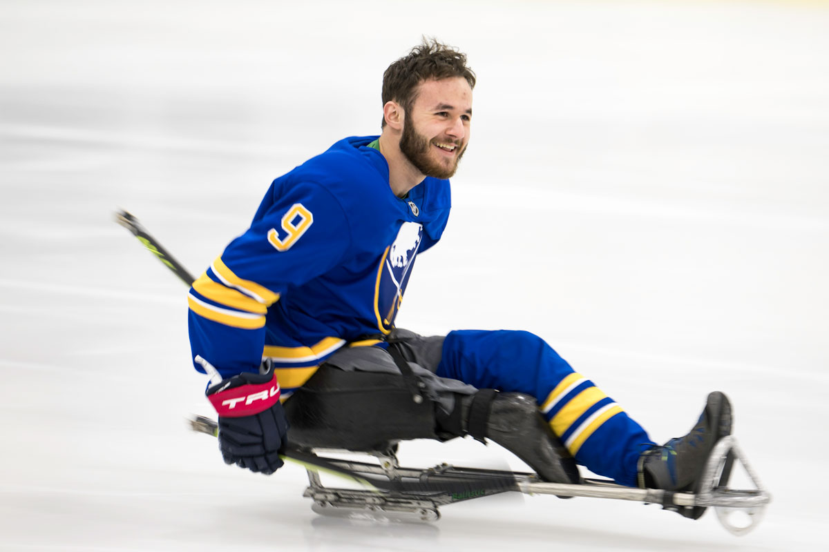 A University of Rochester Class of 2025 student, Sam Becker, sits on a skateboard wearing a blue jersey.