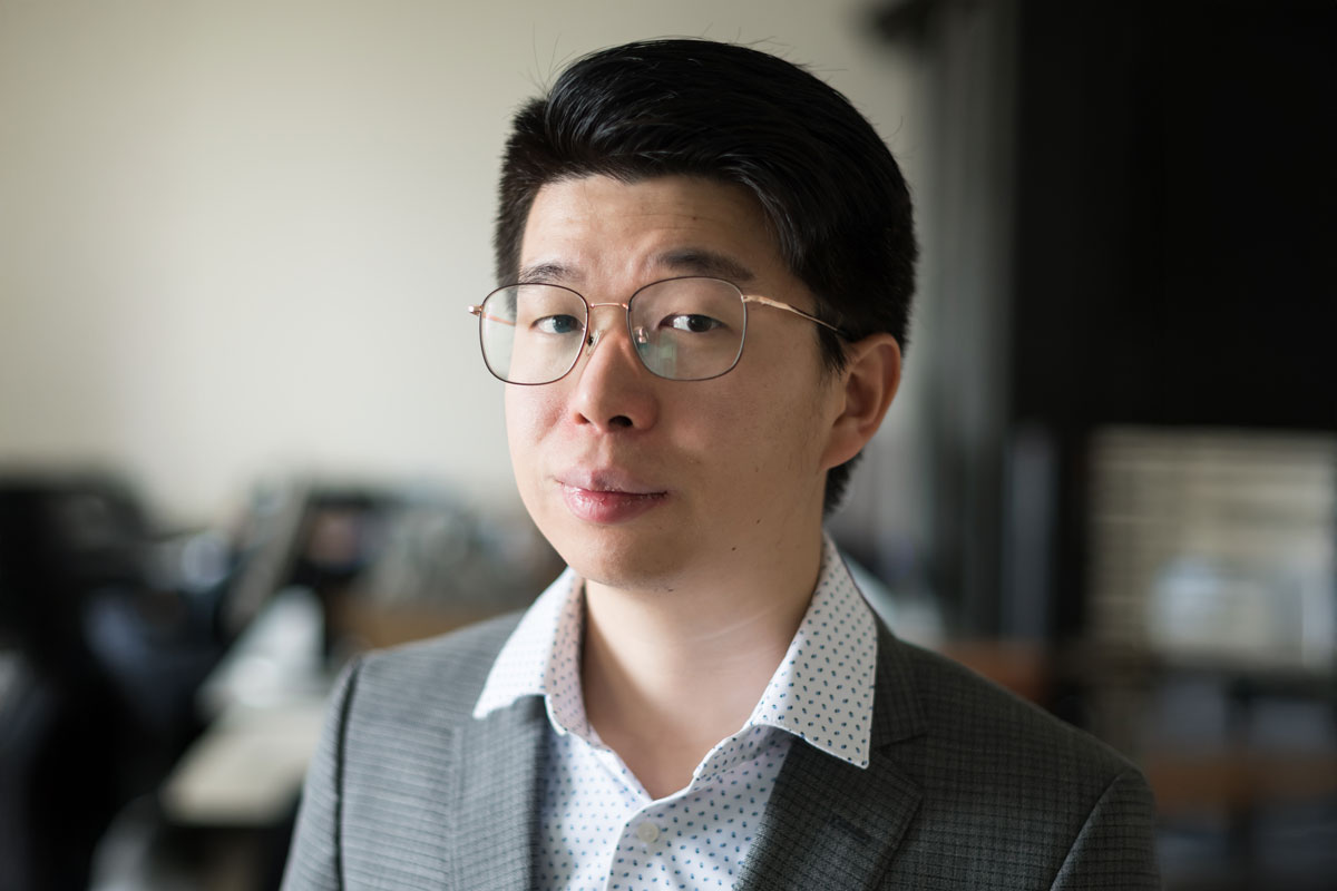 A man in glasses and a suit, Neil Zhang, a University of Rochester Class of 2025 student, is looking at the camera.
