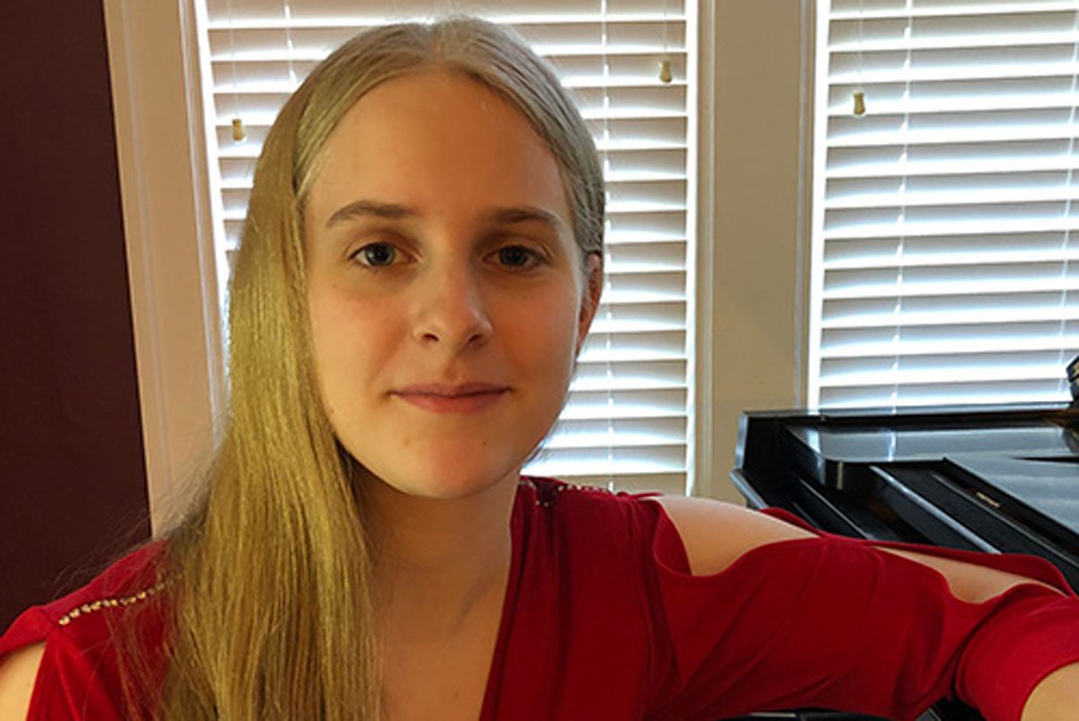 A University of Rochester Class of 2025 student, Katherine Jolliff, sits at a piano wearing a red dress.