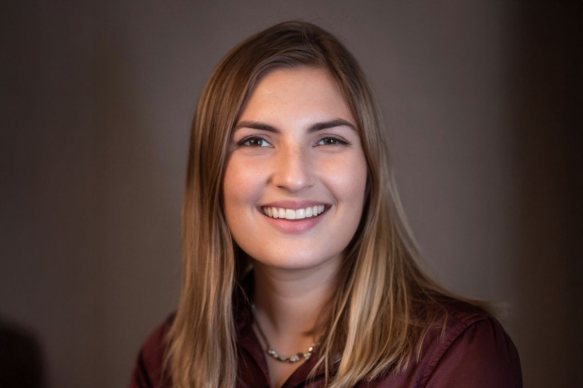 Caitlin Sharp, a University of Rochester Class of 2025 student, with long hair wearing a maroon shirt.