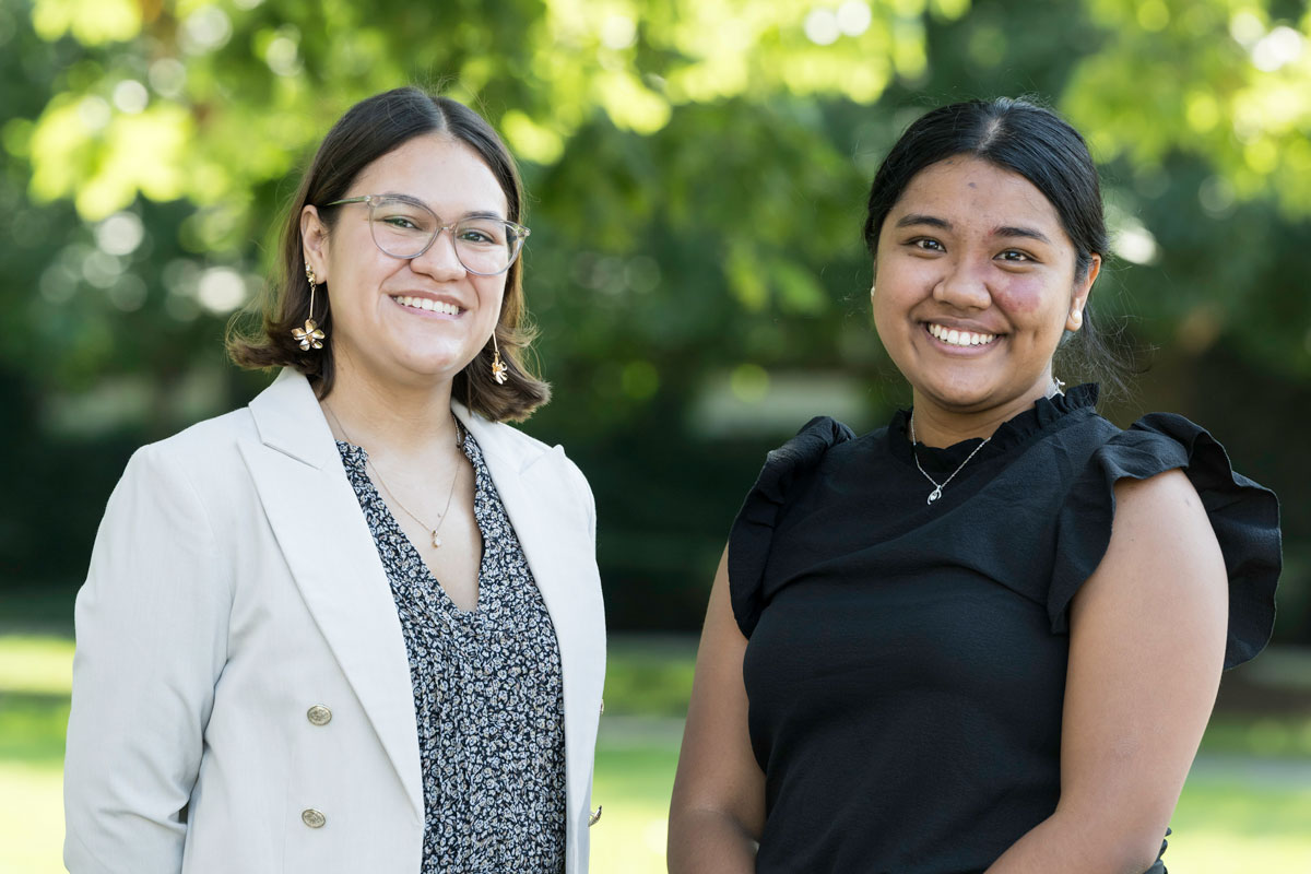 Two women, Mara Criollo-Rivera and Kristel Kezia Layugan, stand together in front of trees at the University of Rochester.