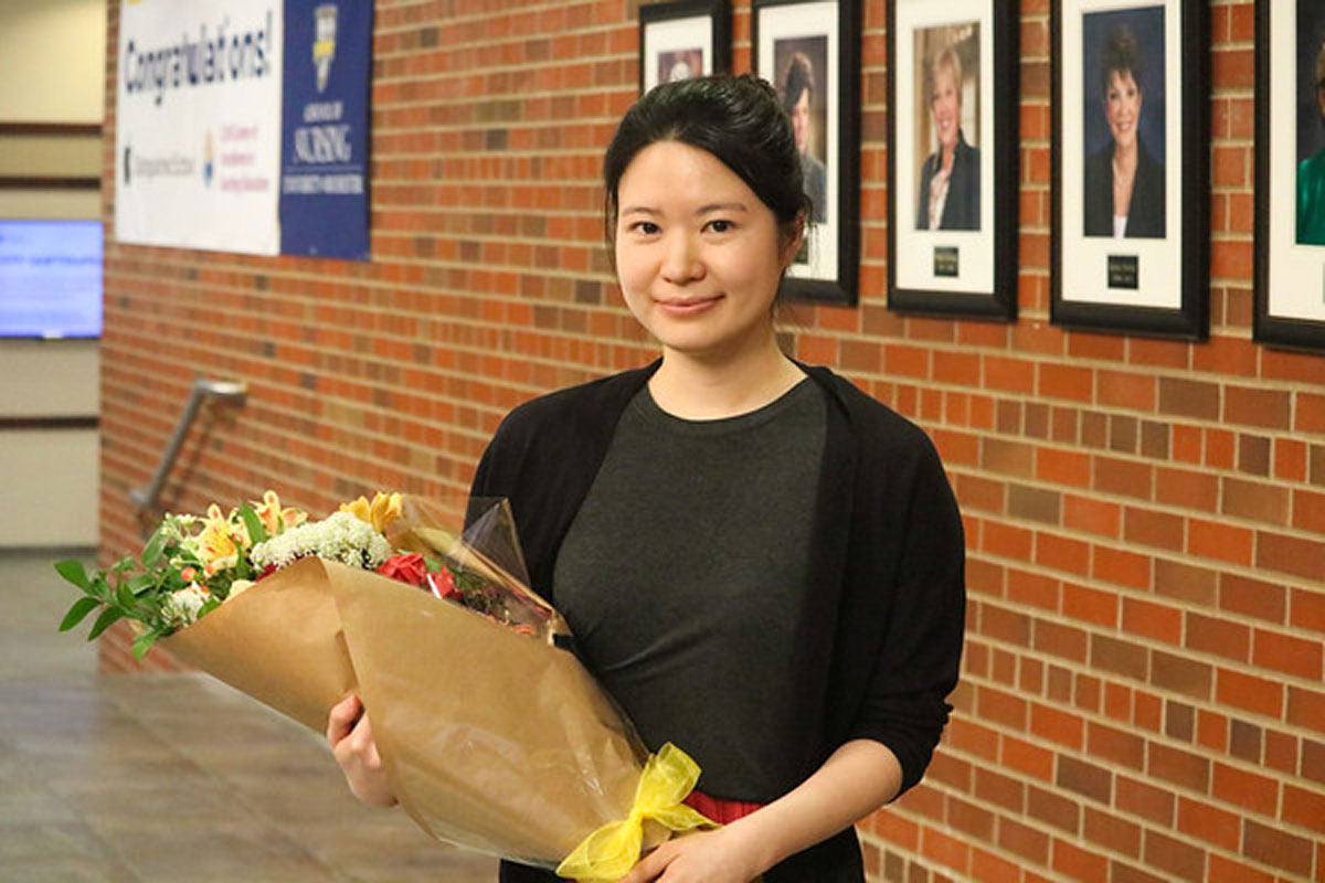 A University of Rochester Class of 2025 student, Wonkyung Chang, holds flowers in front of a textured brick wall.