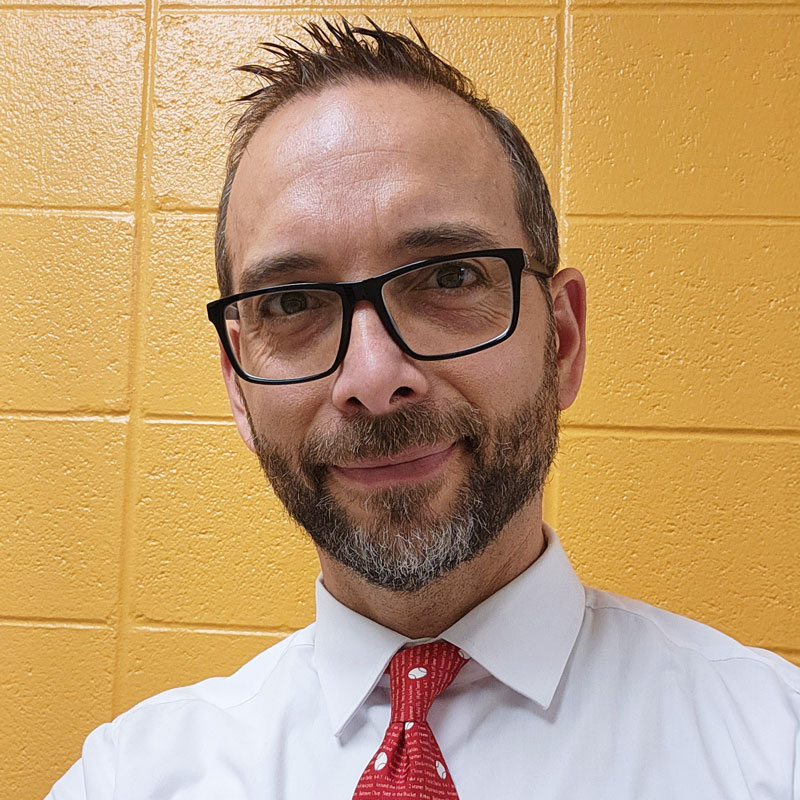 A man with glasses and a red tie, Isaac Perry, a literature and computer science teacher at Lakeland High School.