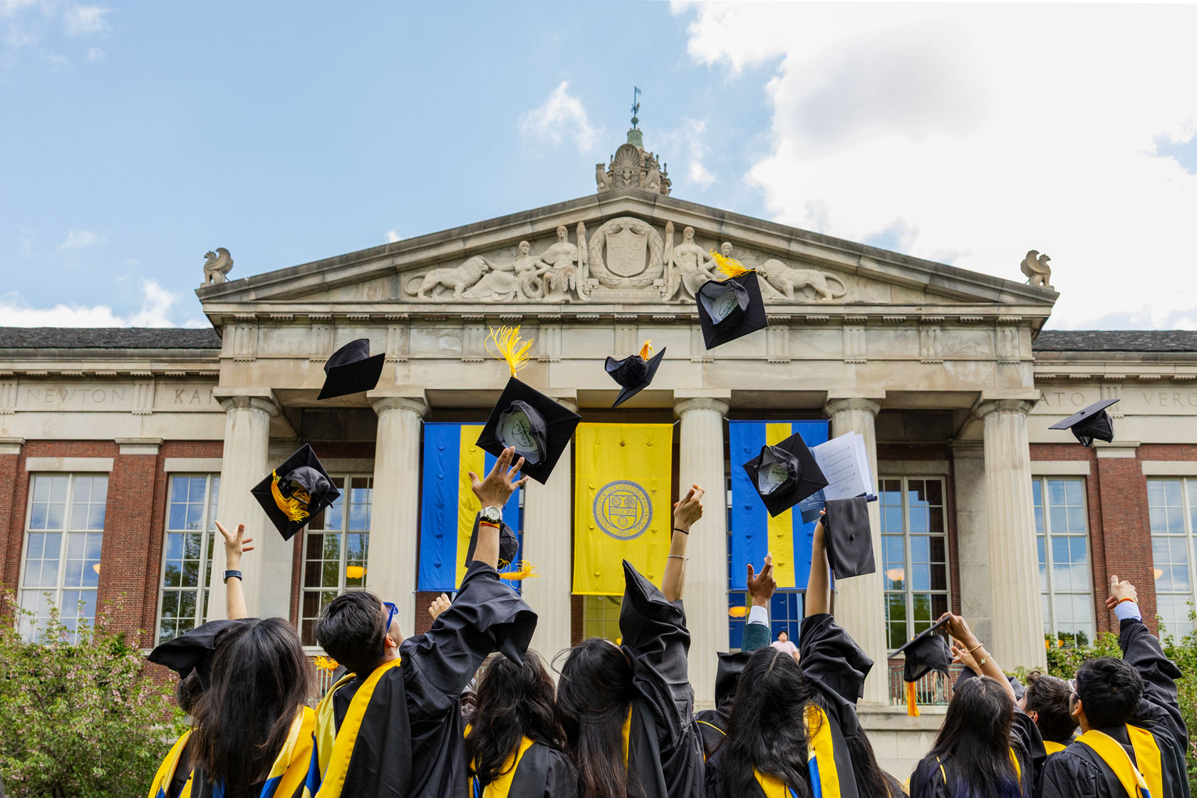 Graduates in caps and gowns joyfully hold their caps aloft after the University of Rochester Commencement ceremony.