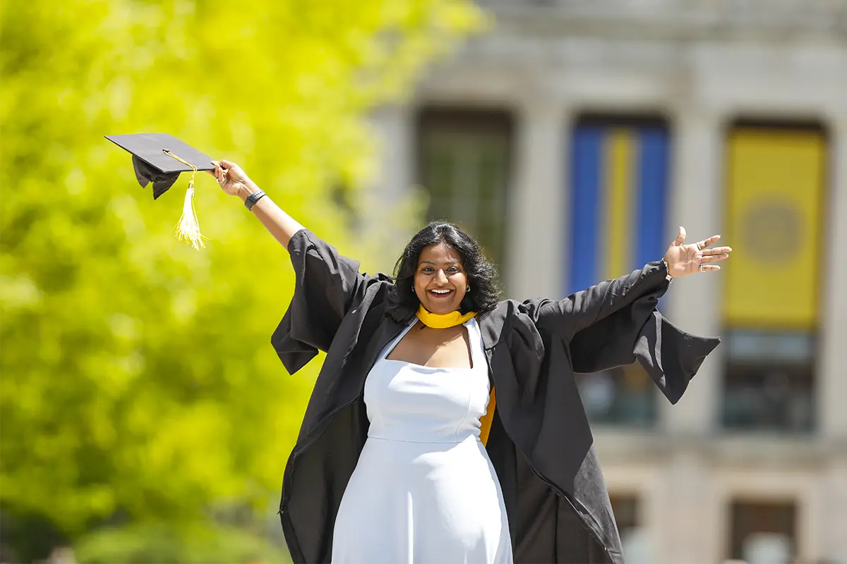 A University of Rochester graduate in a gown and cap joyfully celebrates her achievement.