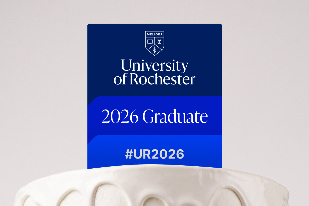 A white cake topped with a blue and white "Commencement 2026" cake topper.
