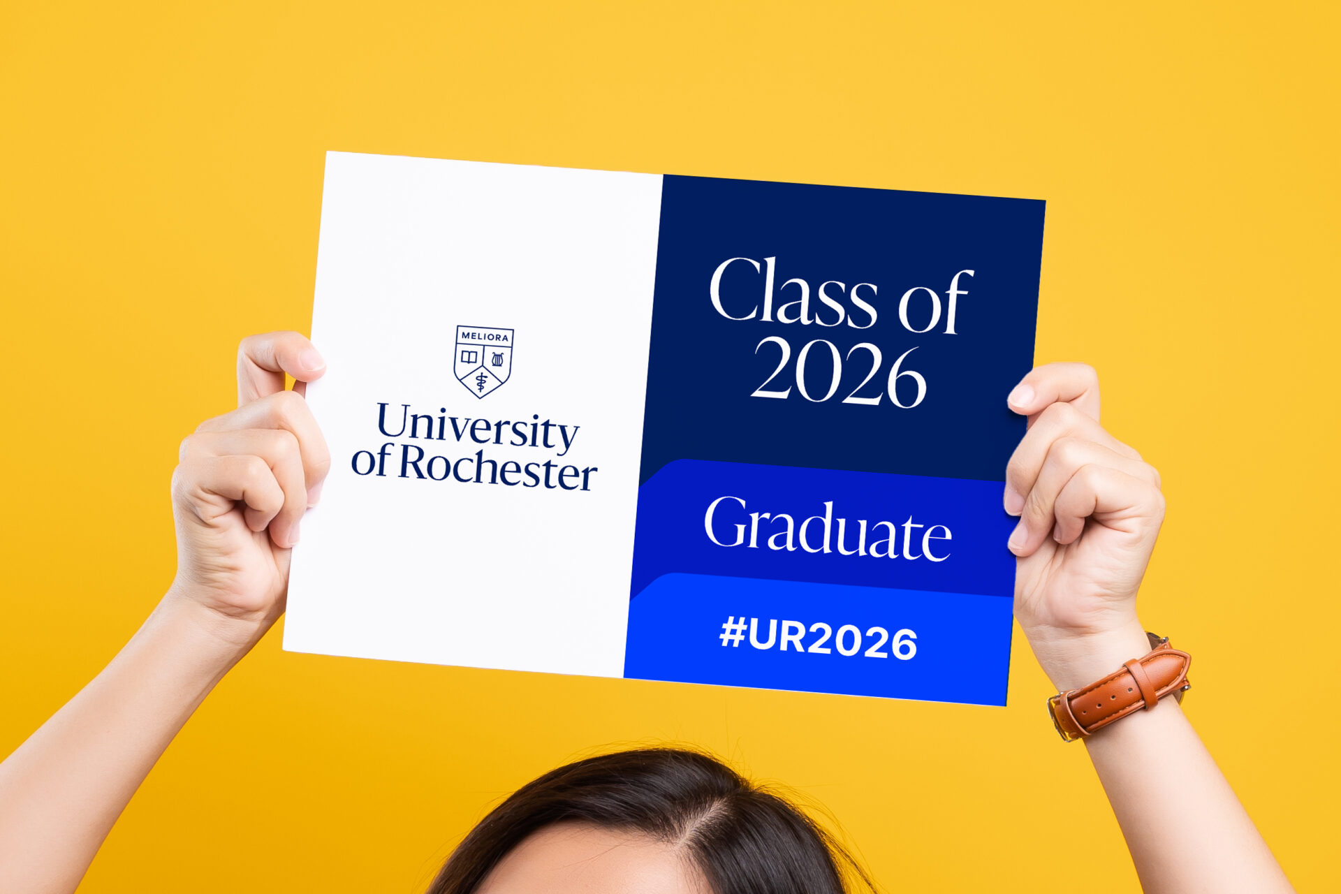 A person displays a sign that says "Class of 2026" while taking a selfie at their Commencement 2026 ceremony.