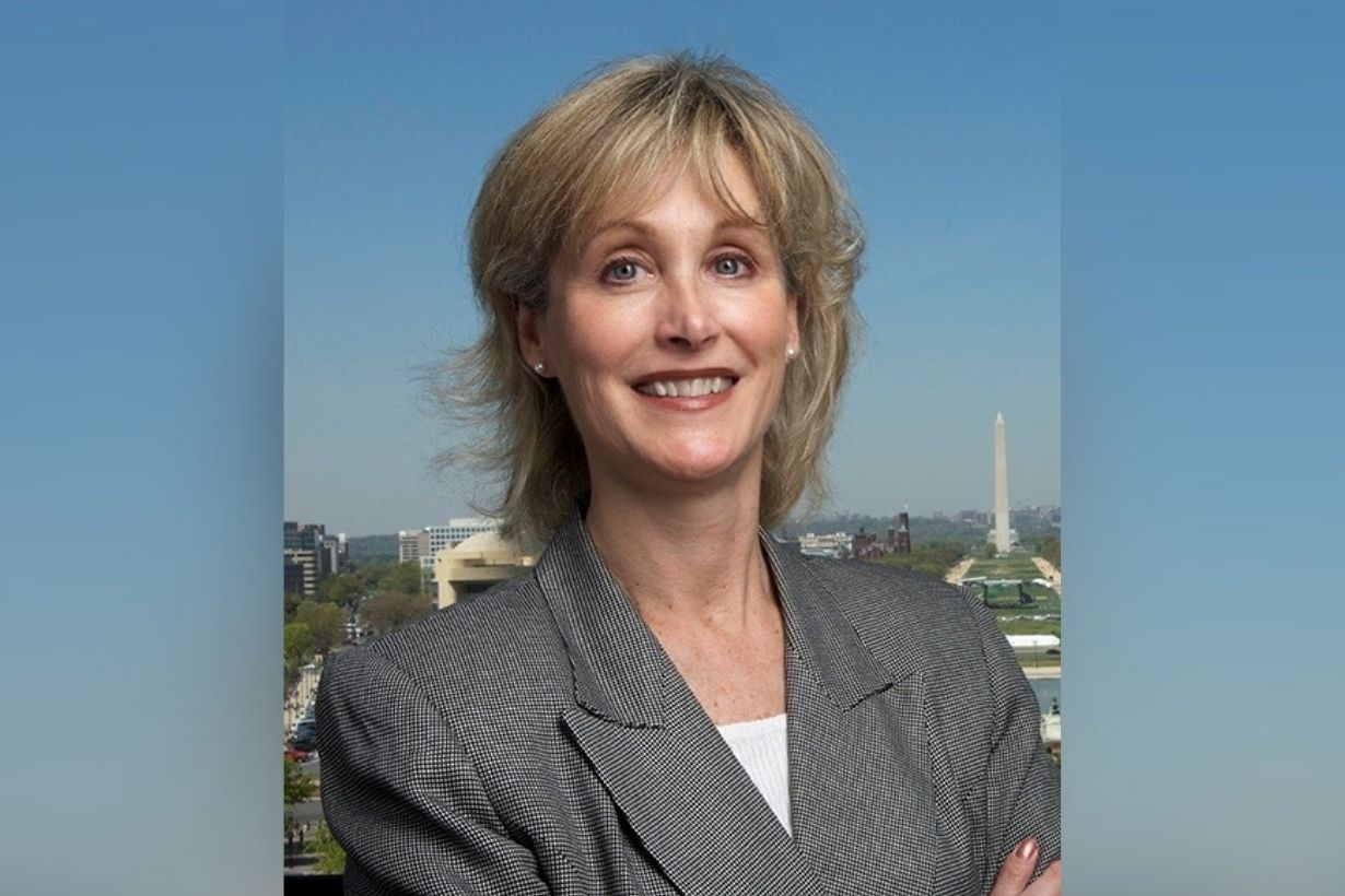 Deborah Trautman headshot: a woman with blond hair wearing a gray blazer, with a blue sky behind her