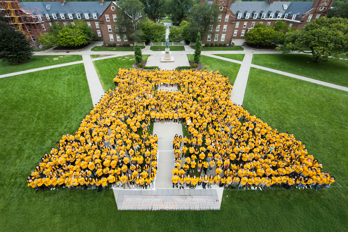University of Rochester Class of 2027 students wearing yellow shirts pose together in the shape of a large “R” on Wilson Quad.