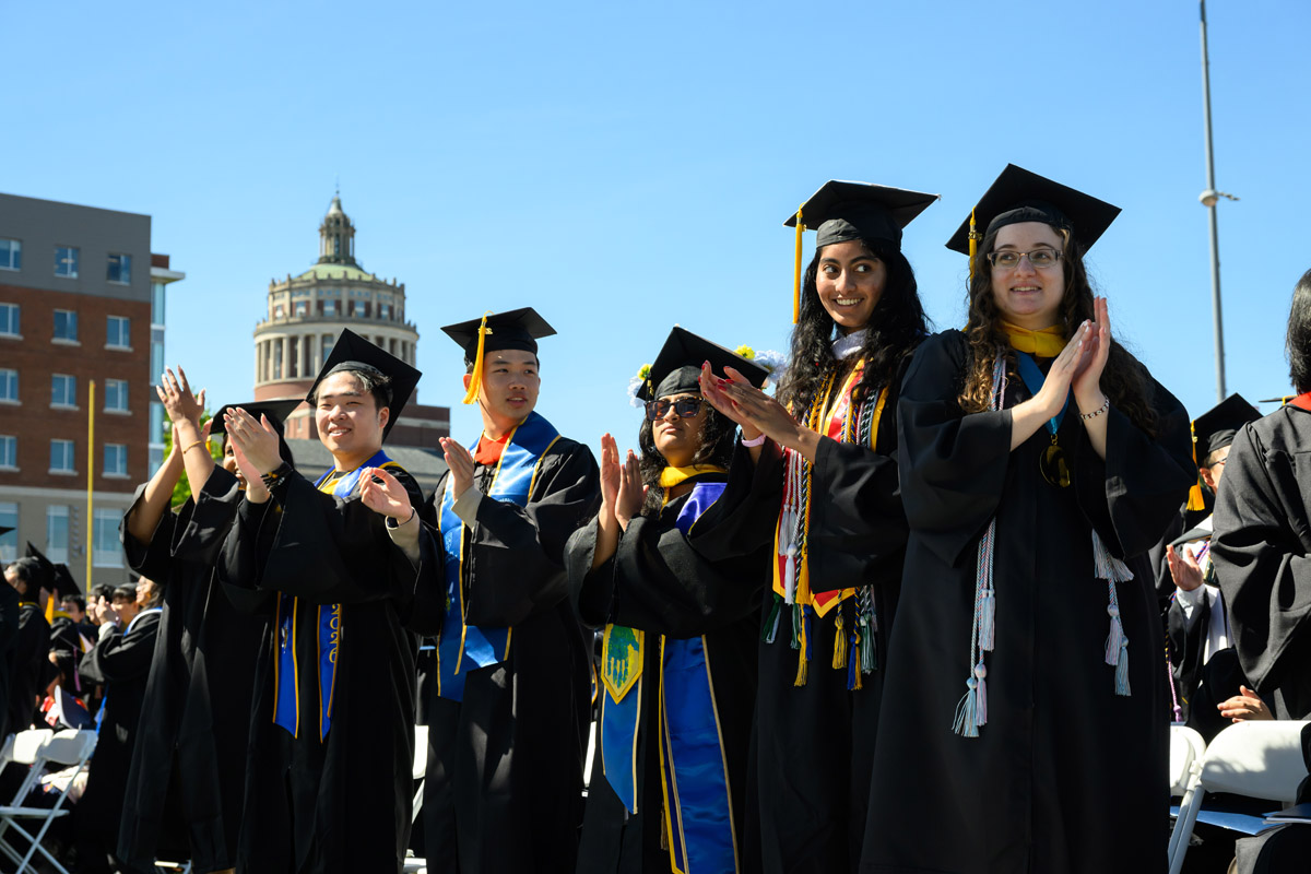University of Rochester graduates applaud with Rush Rhees Library in the background during Commencement Weekend.