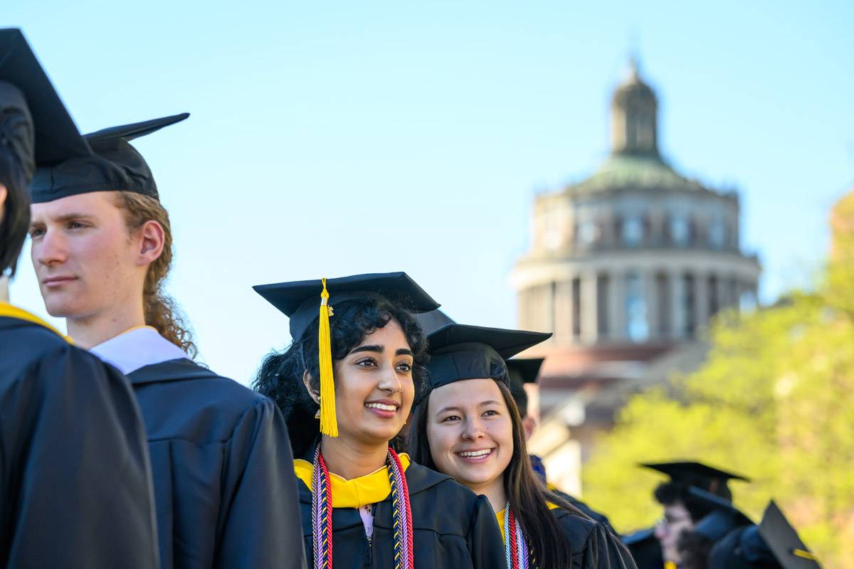 University of Rochester graduates stand together during Commencement Weekend with Rush Rhees Library in the background.