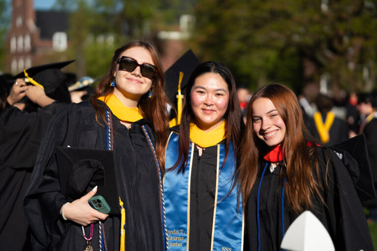 Three University of Rochester graduates pose together in academic regalia during Commencement Weekend.