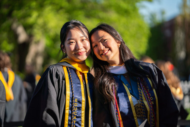 Two University of Rochester graduates pose together in the sunlight during Commencement Weekend.