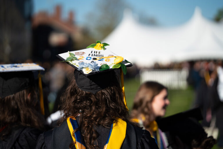 A University of Rochester graduate wears a decorated cap with flowers and the words Life finds 2026 during Commencement Weekend.