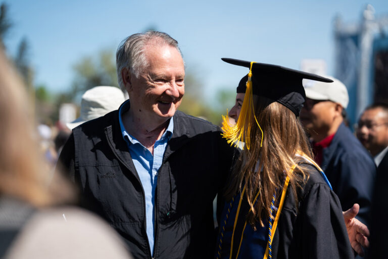 University of Rochester faculty stand in blue doctoral regalia with Rush Rhees Library in the background.