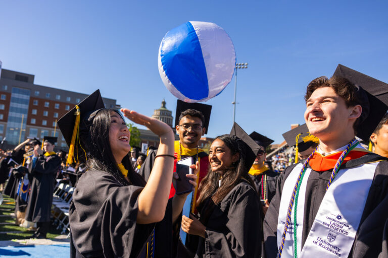 University of Rochester graduates play with a beach ball during the Commencement Weekend ceremony at Fauver Stadium.