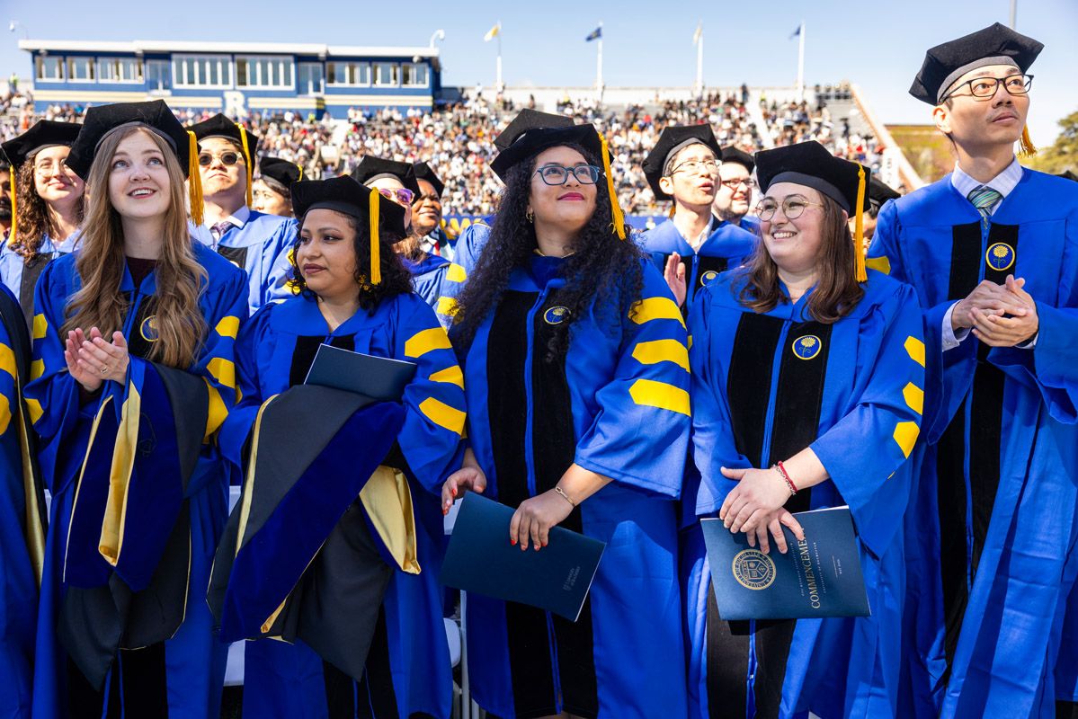 University of Rochester graduates in blue doctoral regalia stand and applaud during Commencement Weekend.
