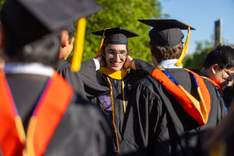 A University of Rochester graduate smiles while adjusting his academic hood during Commencement Weekend.
